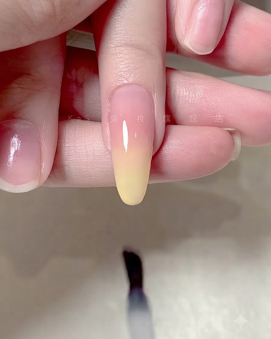 A brush applying a clear glossy top coat over an ombre gradient nail design.