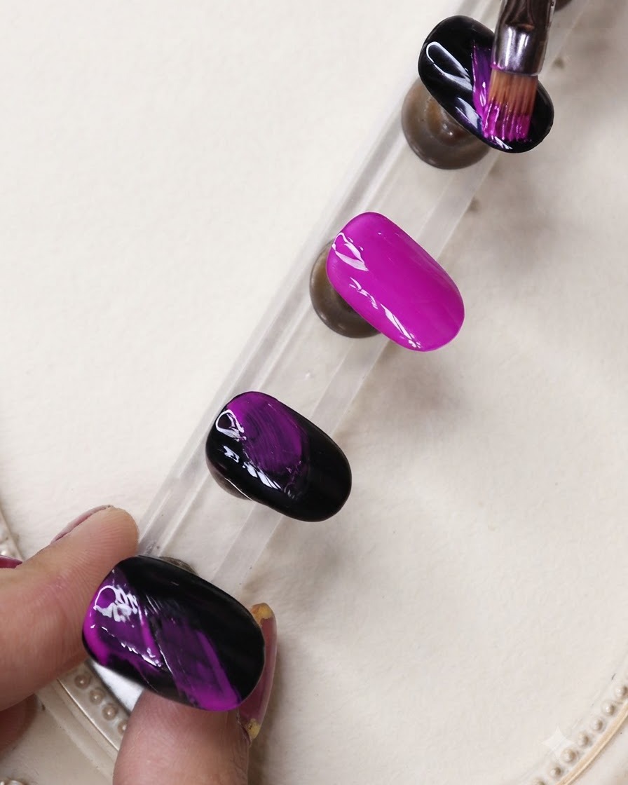 A fine liner brush applying black gel streaks over a vibrant neon purple nail on a display stand.