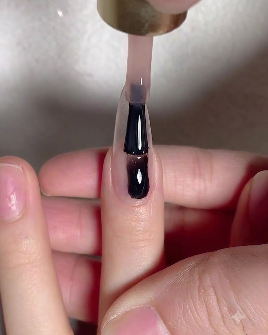 A gel brush applying a smooth layer of nude base gel down the center of an elongated natural nail plate.