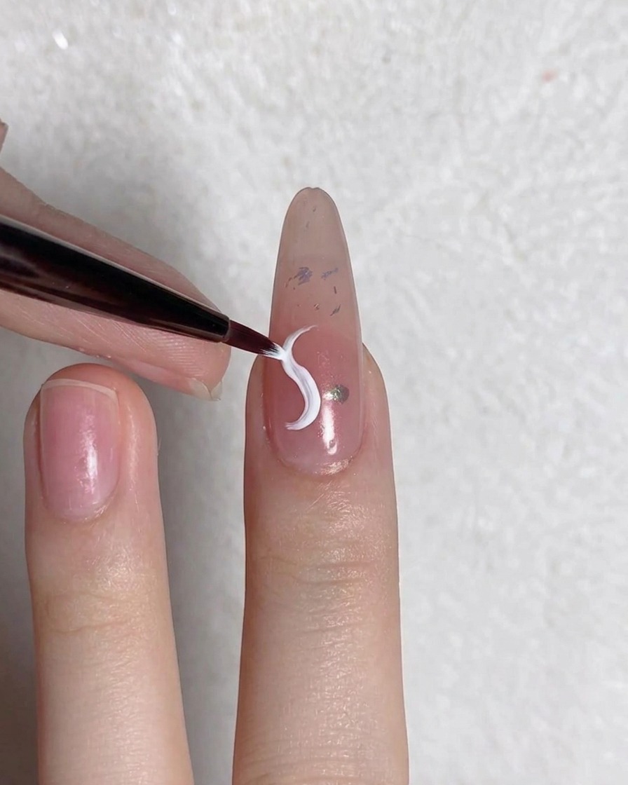 A fine liner brush drawing a white curved petal line onto a prepped nail.