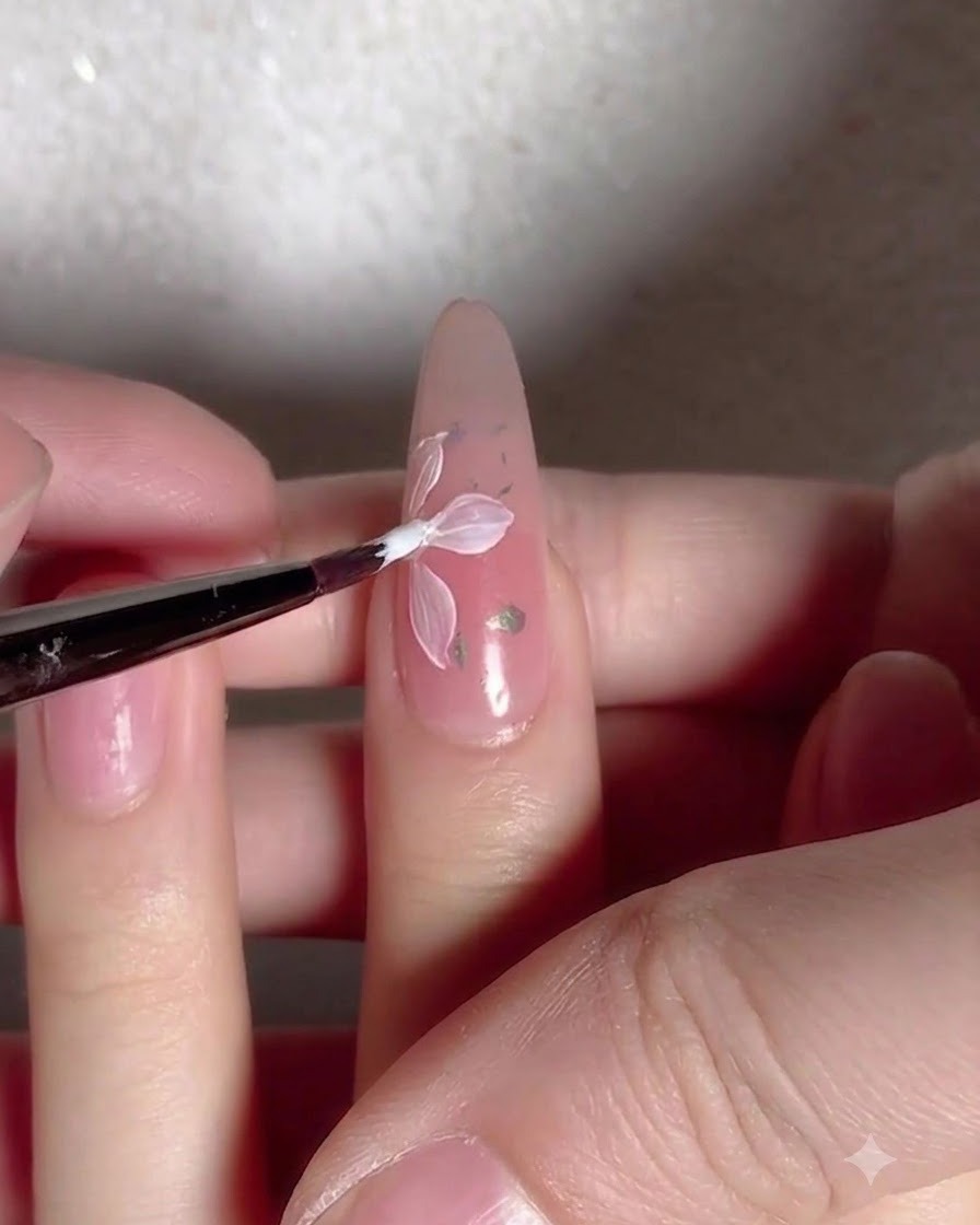 A brush applying a clear glossy top coat layer over a nail decorated with flowers and flakes.