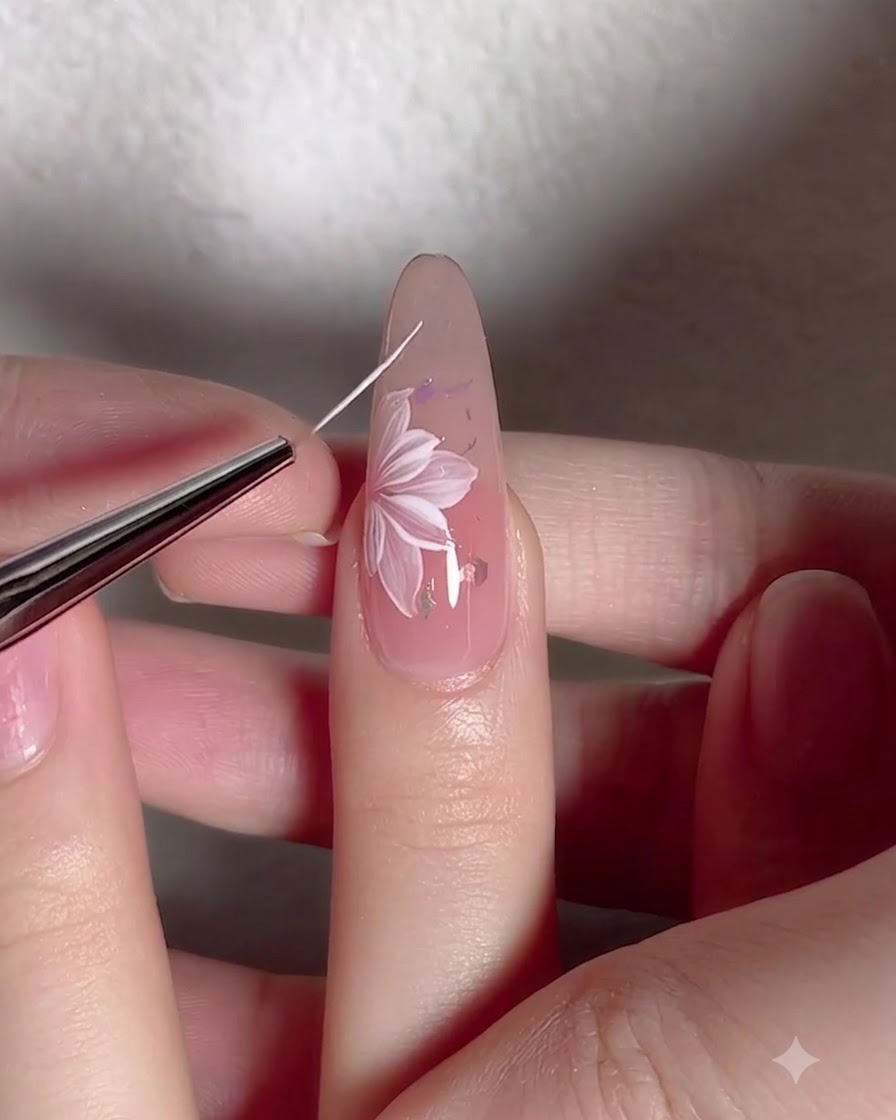 A fine liner brush drawing delicate white vine lines around a painted flower on a nail.