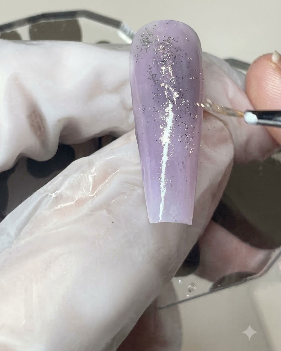 A gel brush applying a smooth coat of matte top coat over a glitter-infused purple gradient nail.