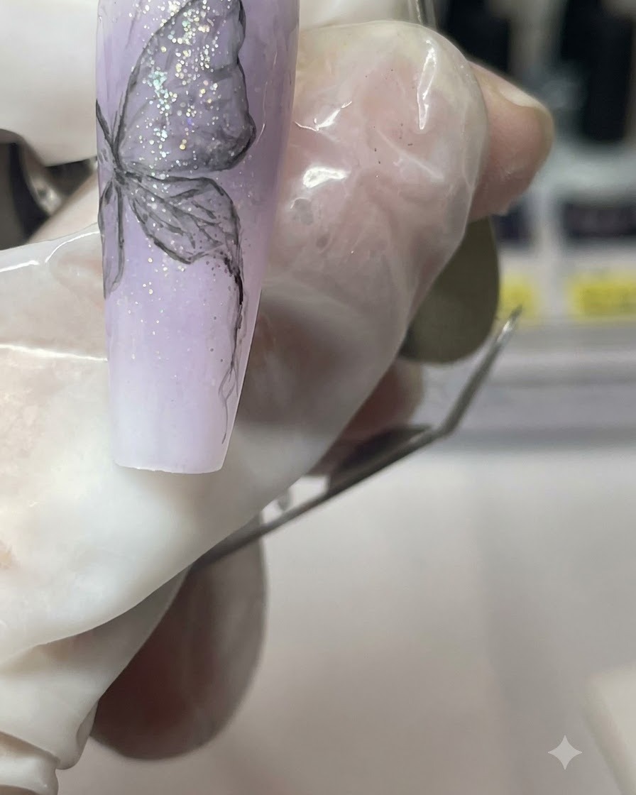 A close-up of a manicured finger holding the purple nail tip while detailing the butterfly body.