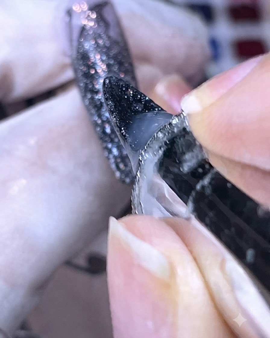 A close-up view of base glue being applied around the edges of a dark sparkly nail tip.