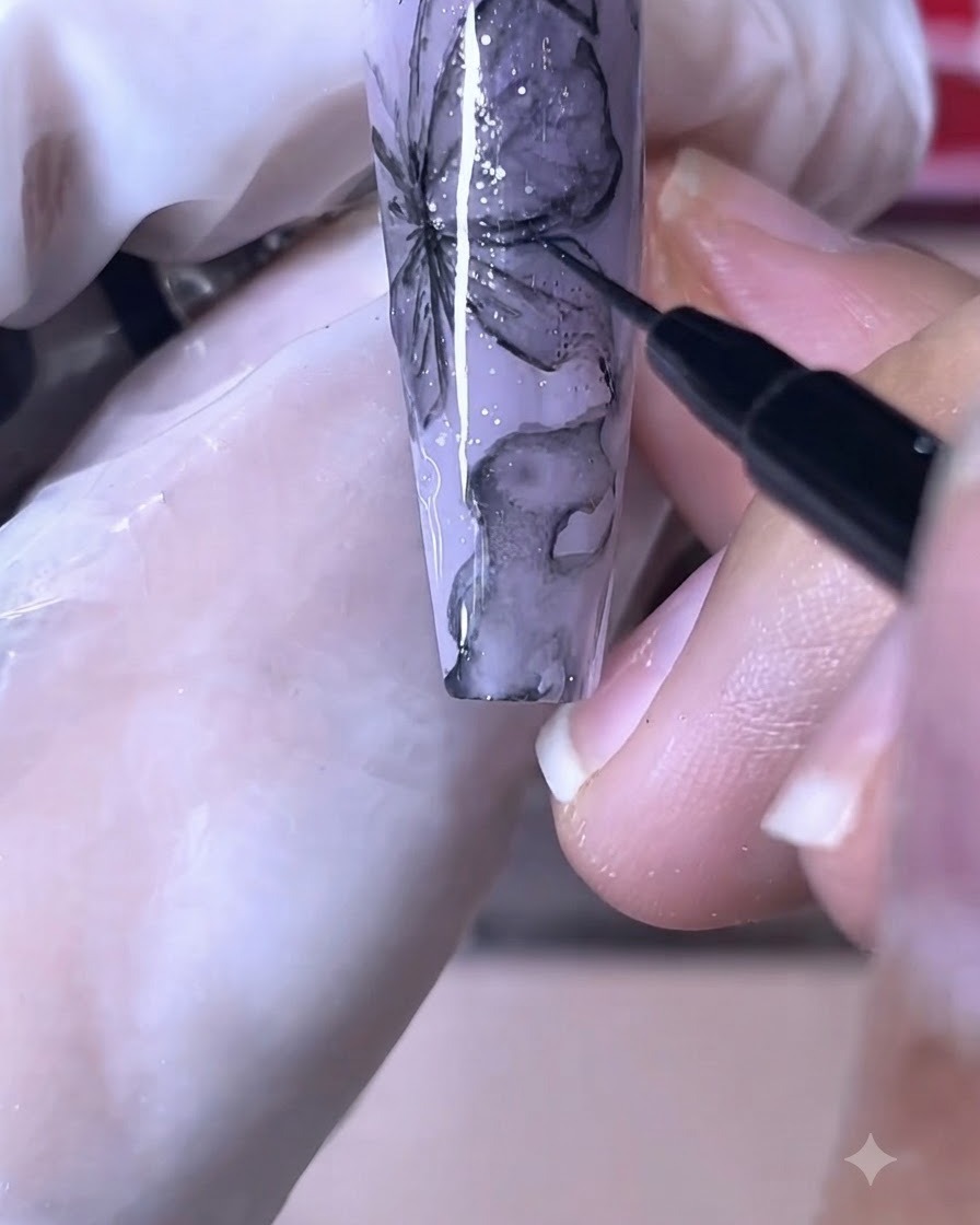 A fine nail brush drawing crisp black lines onto a purple butterfly nail design.