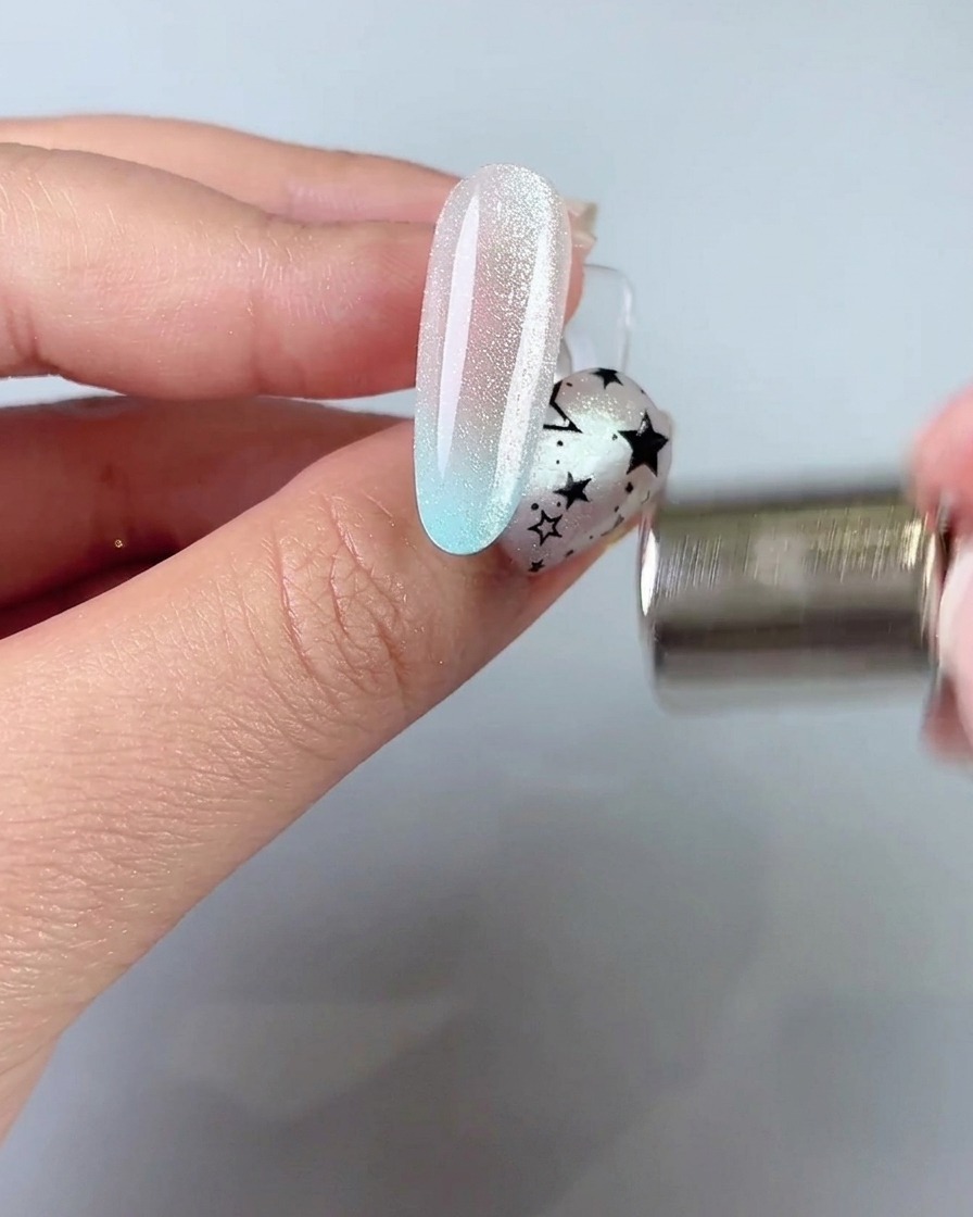 A magnetic wand held near the side of a nail to pull and shape a wide cat eye light band.