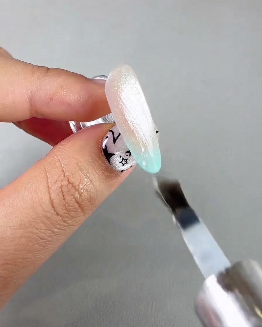 A nail brush applying a clear sealing top coat over a shimmering cat eye nail extension.