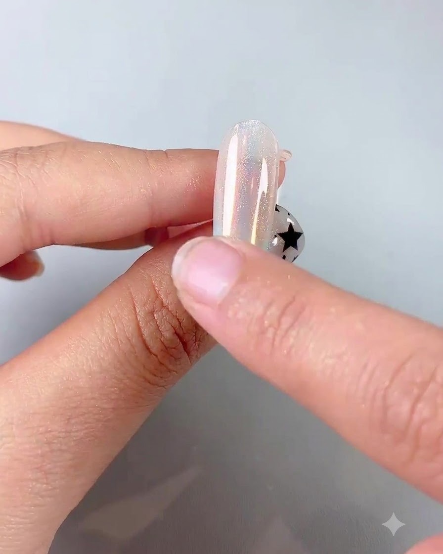 A finger using a silicone sponge applicator to rub iridescent chrome powder onto a glossy nail.