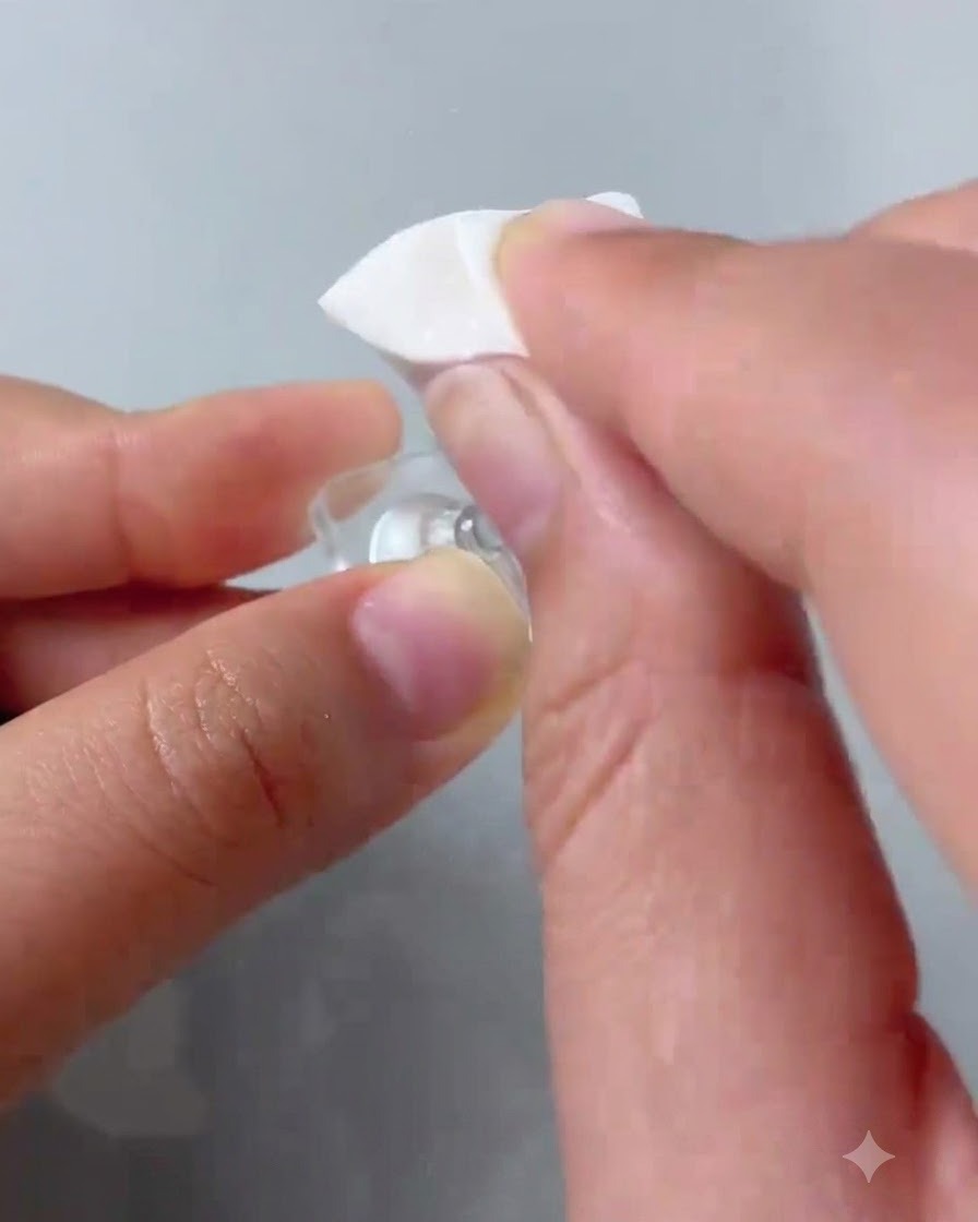 A sponge applicator dabbing pink gel polish onto the tip of a clear practice nail.
