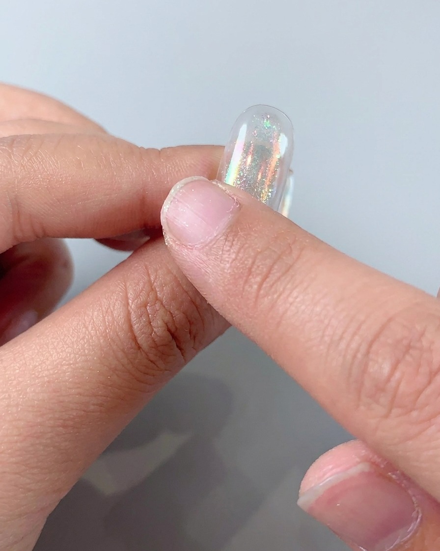 Rubbing holographic aurora powder onto a nail to create a shiny metallic finish.