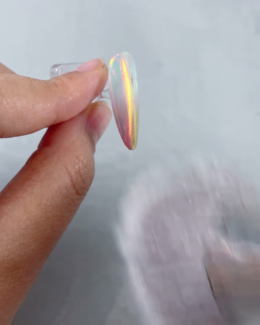 A soft fluffy brush sweeping away residual metallic powder from a shiny chrome-finished nail.