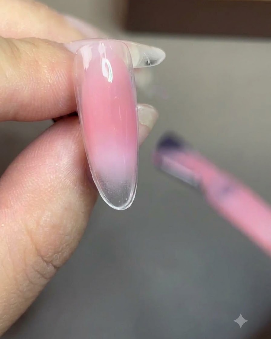 A brush applying a sheer nude gel polish evenly over the entire nail.