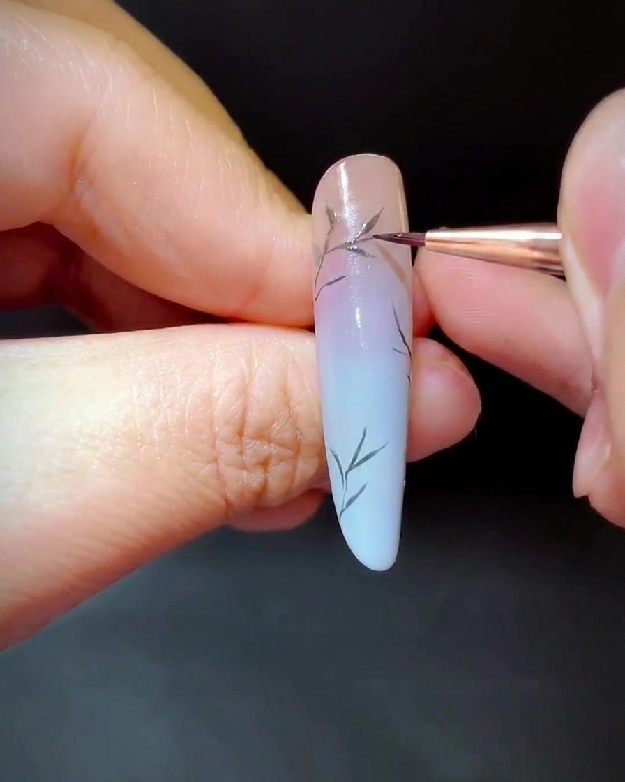 A detailer brush painting tiny green leaves along the lower sections of the nail branches.