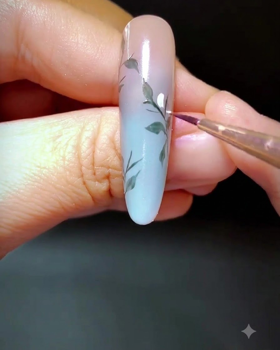 A close-up of a decorated nail where white gel dots are being applied along the painted branch.