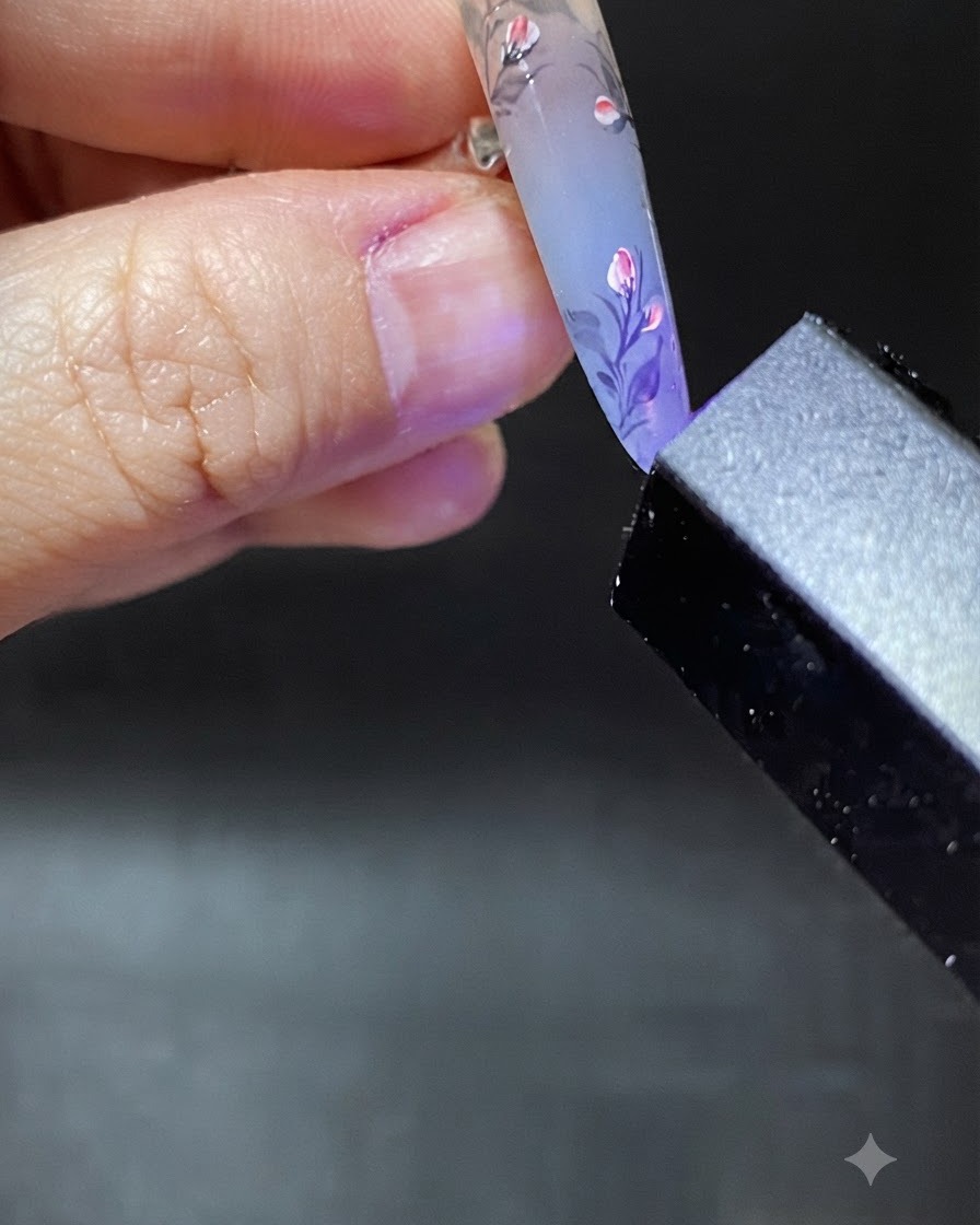A brush applying a clear blob of reinforcement gel near the cuticle area of the decorated nail.