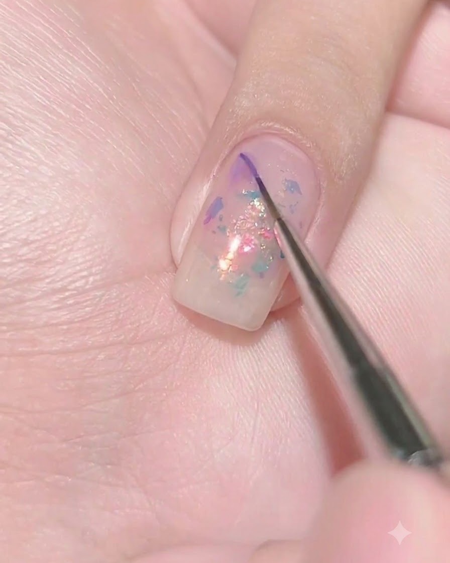 A fine liner brush depositing a tiny dot of dark purple gel onto the wet surface of a sheer purple nail.