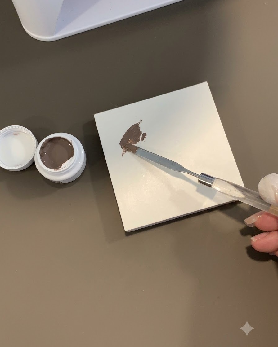 A sponge tool dabbing into a patch of brown-grey gel on a white tile surface.