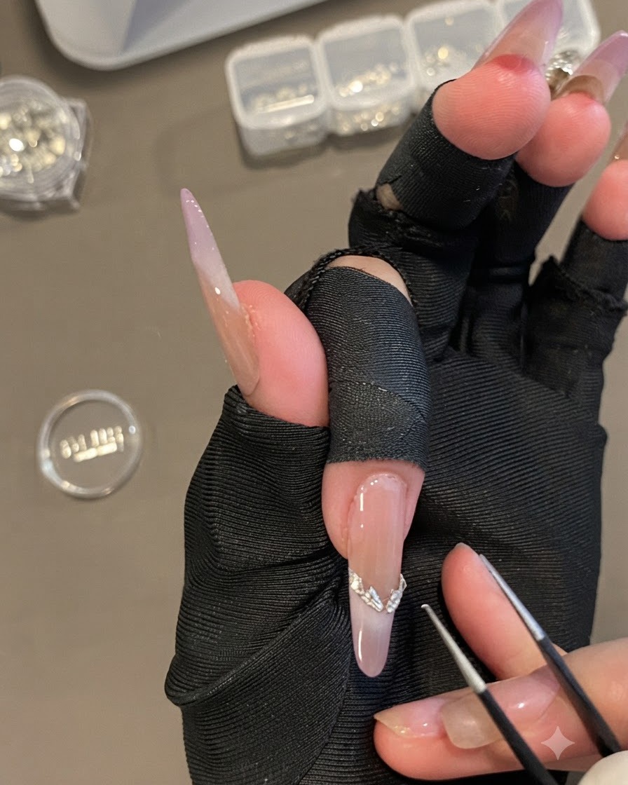 A hand holding fine tweezers placing a curved silver French tip sticker onto a long oval nail.