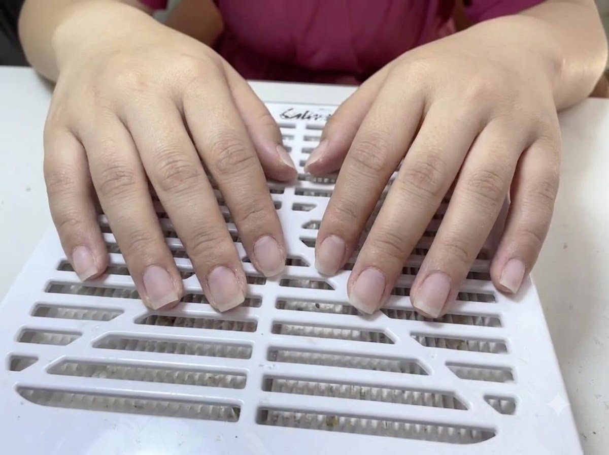 Two hands with bare, unpolished natural nails resting on a white slotted dust collector surface.