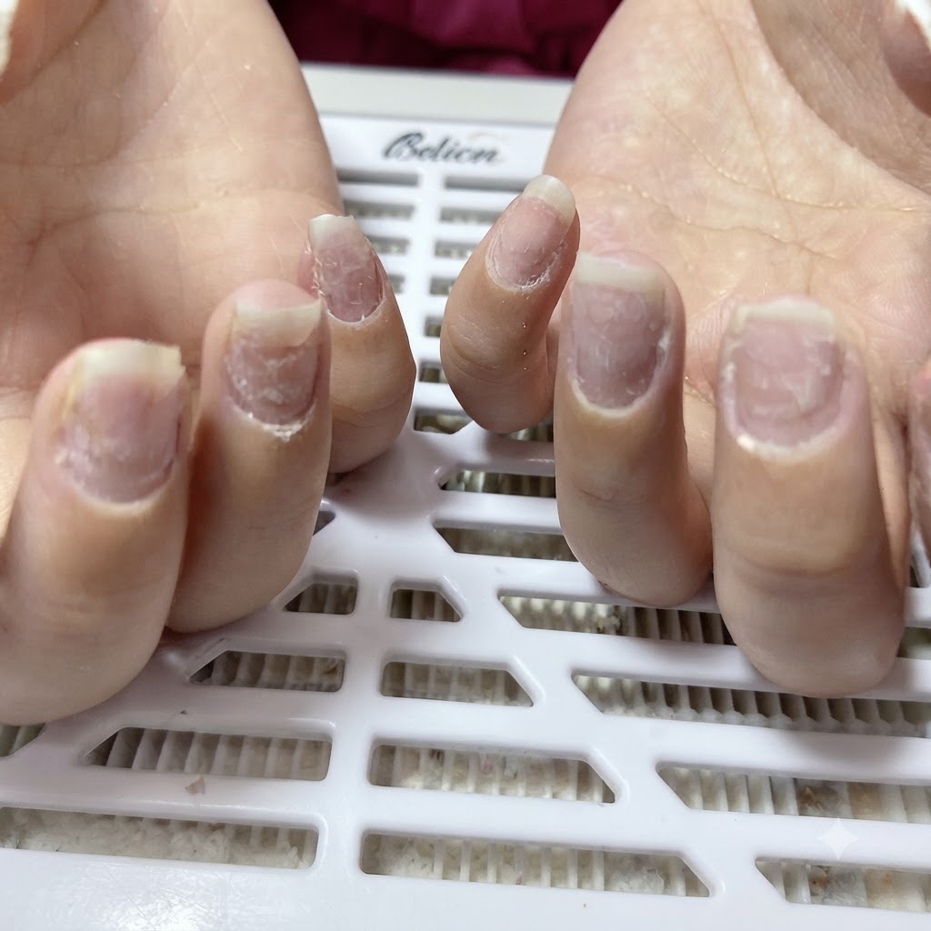 Close-up of natural fingernails that have been filed into an almond shape, with white nail dust visible around the cuticles and nail folds.