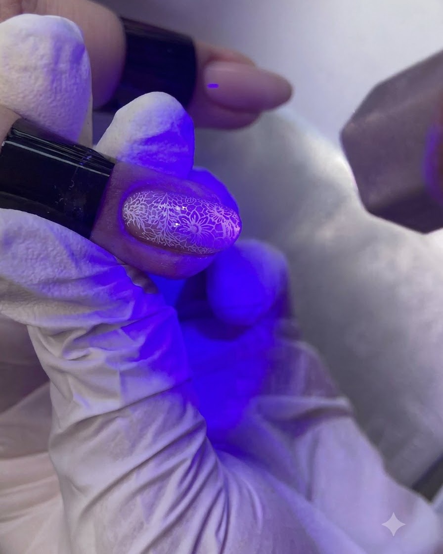 A hand under a purple UV/LED nail lamp curing a decorated fingernail.
