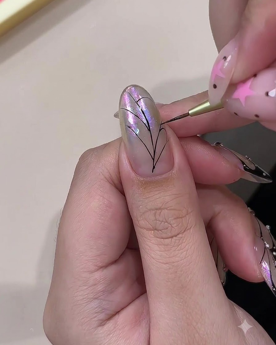 A fine brush painting curved black lines to connect the veins of a butterfly wing pattern on a nail.