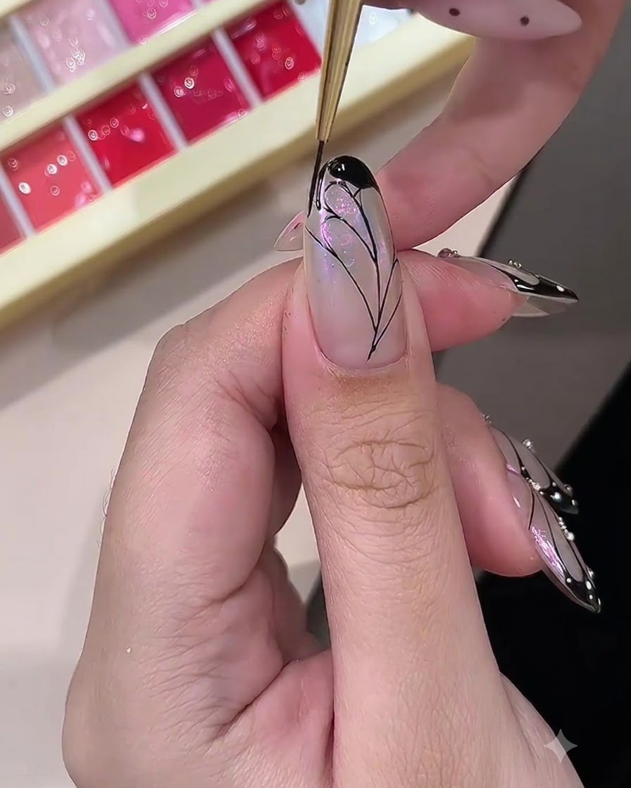 A nail technician filling in the outer borders of a painted butterfly wing design with opaque black gel.