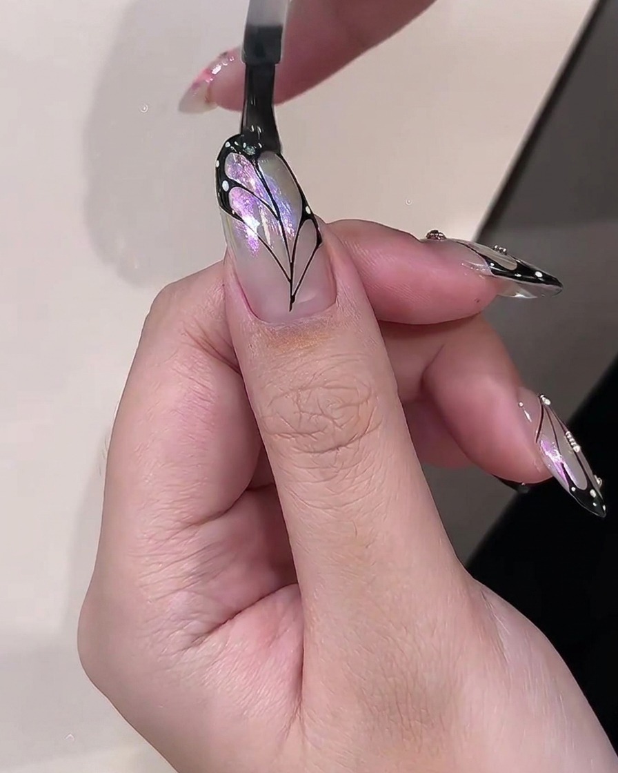 A brush applying clear glossy top coat over a finished butterfly wing nail art design.