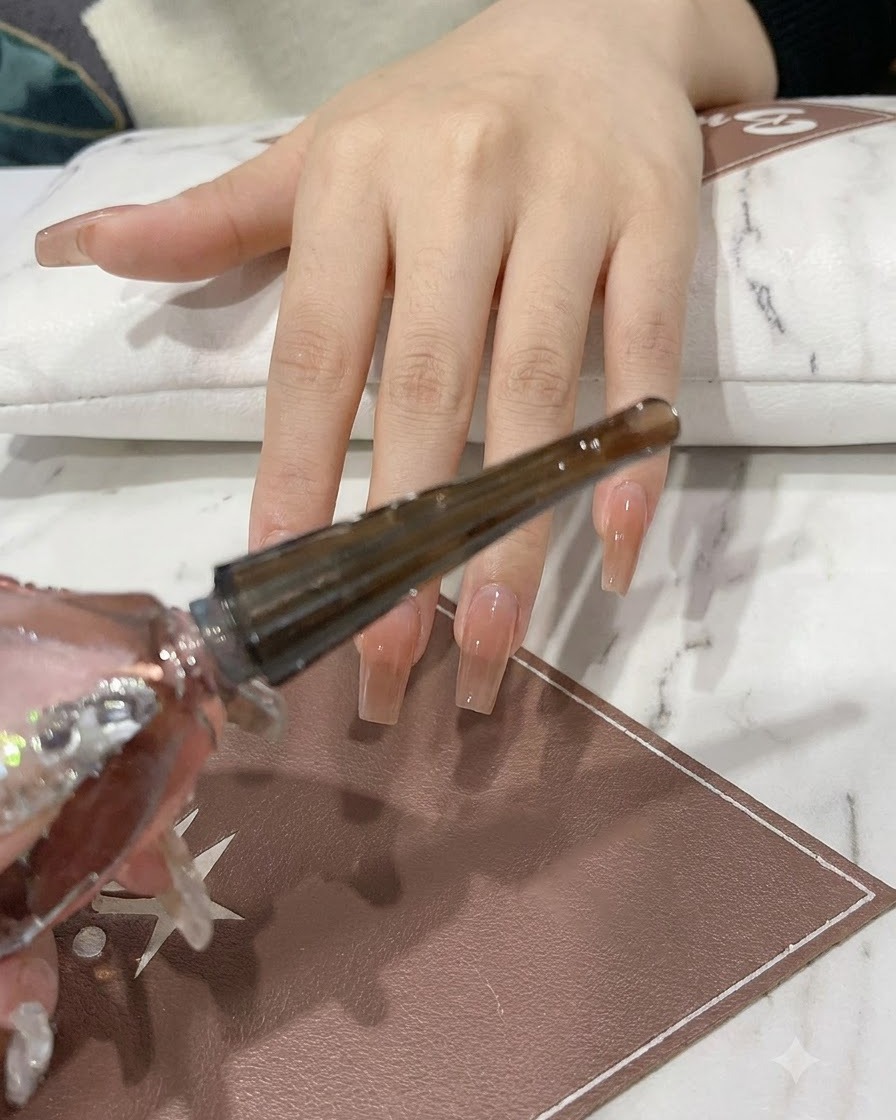 A hand holding a sparkling pink and silver gel bottle with the brush applicator extended.