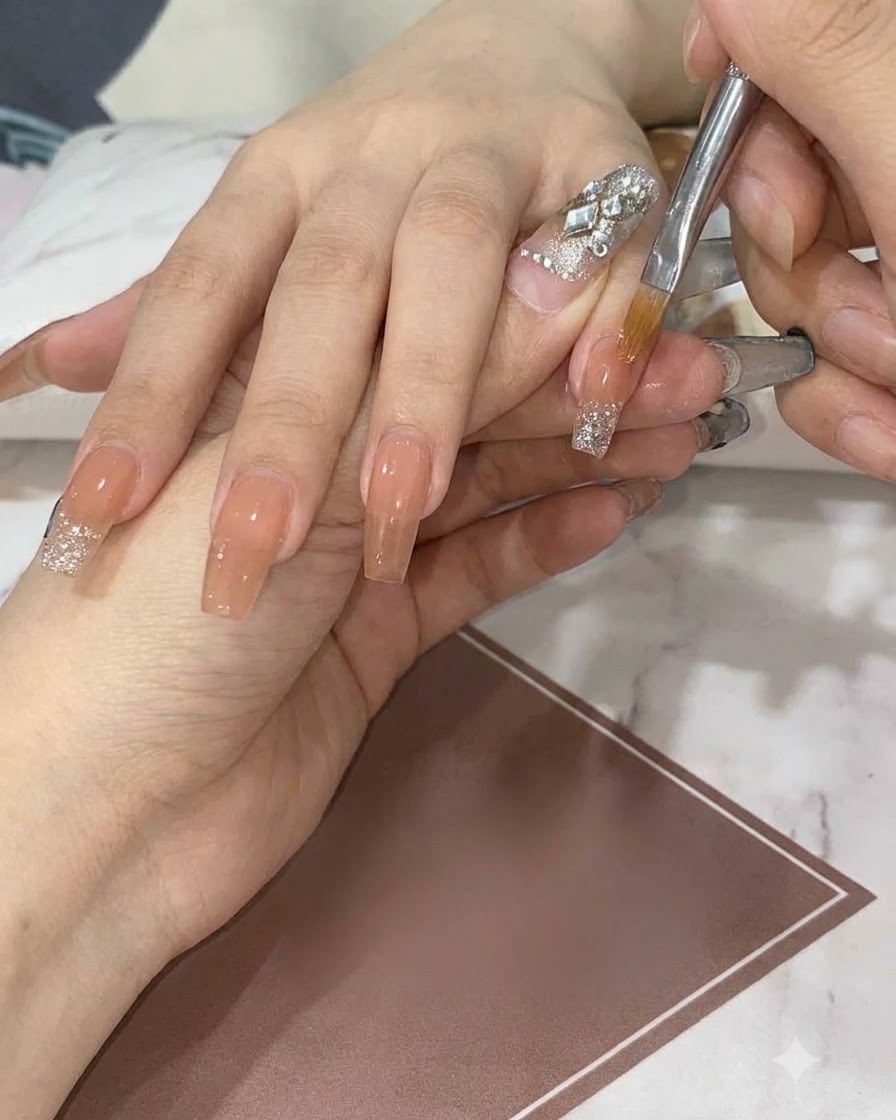 A flat detail brush feathering and dragging silver glitter downward on a nude nail to create a smooth gradient.