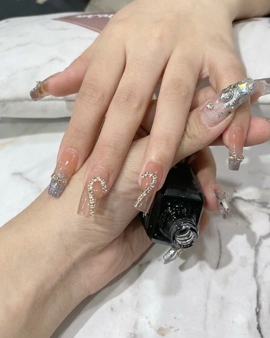 Tweezers placing small sparkling rhinestones inside a metallic chain outline on a fingernail.