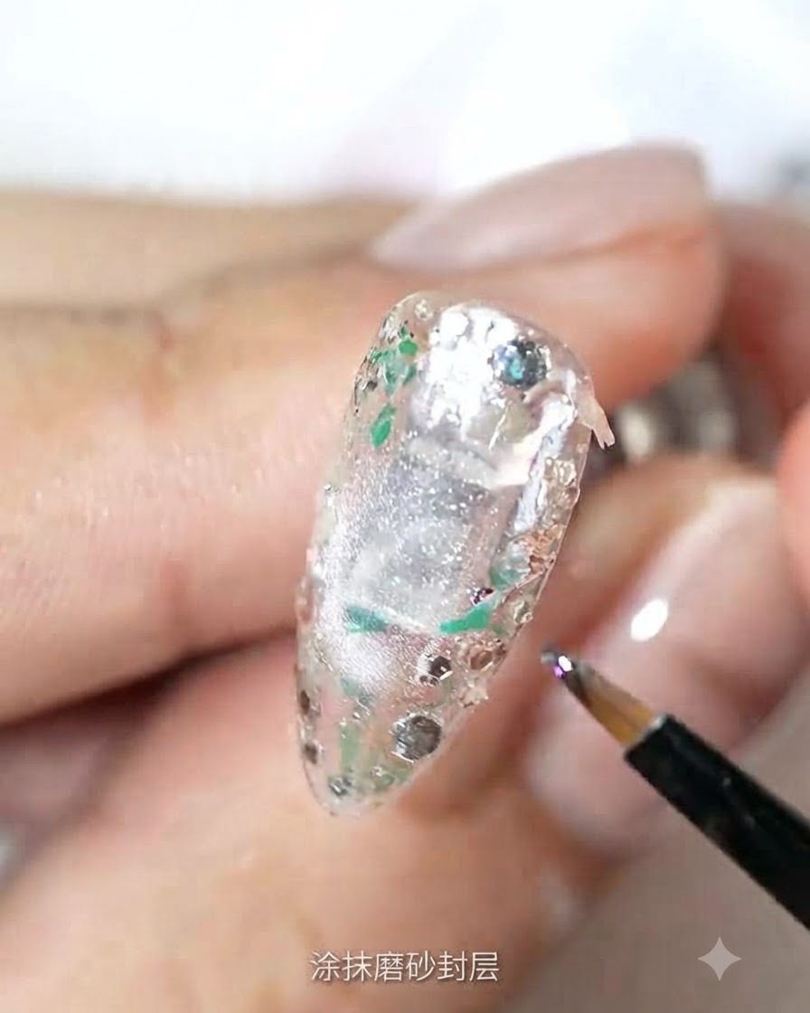A fine brush applying matte top coat over a textured, glitter-embedded nail surface.