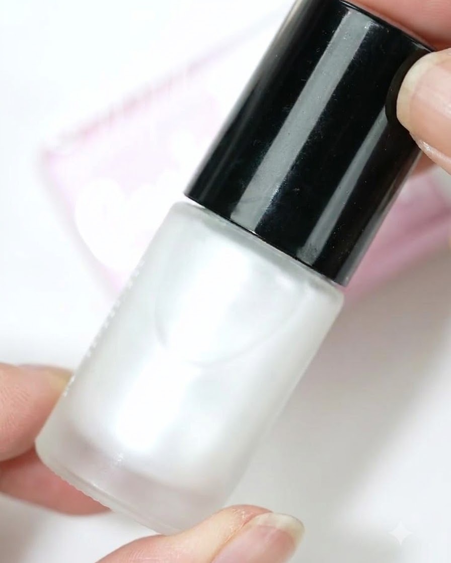 A bottle of pearl white blooming dye held against a light background.