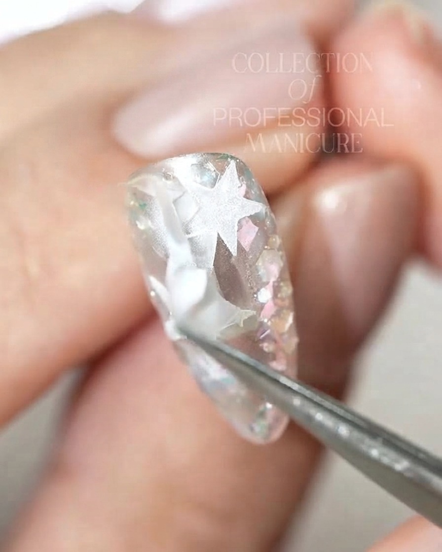 A pair of tweezers peeling off intricate white star sticker pieces from a glossy nail.