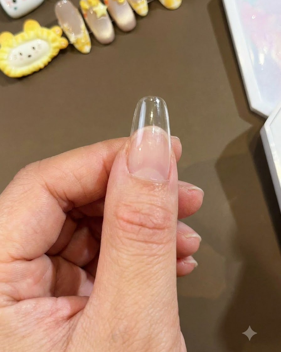 A close-up shot of a clear long almond nail tip held against a thumb, ready for nail art application.