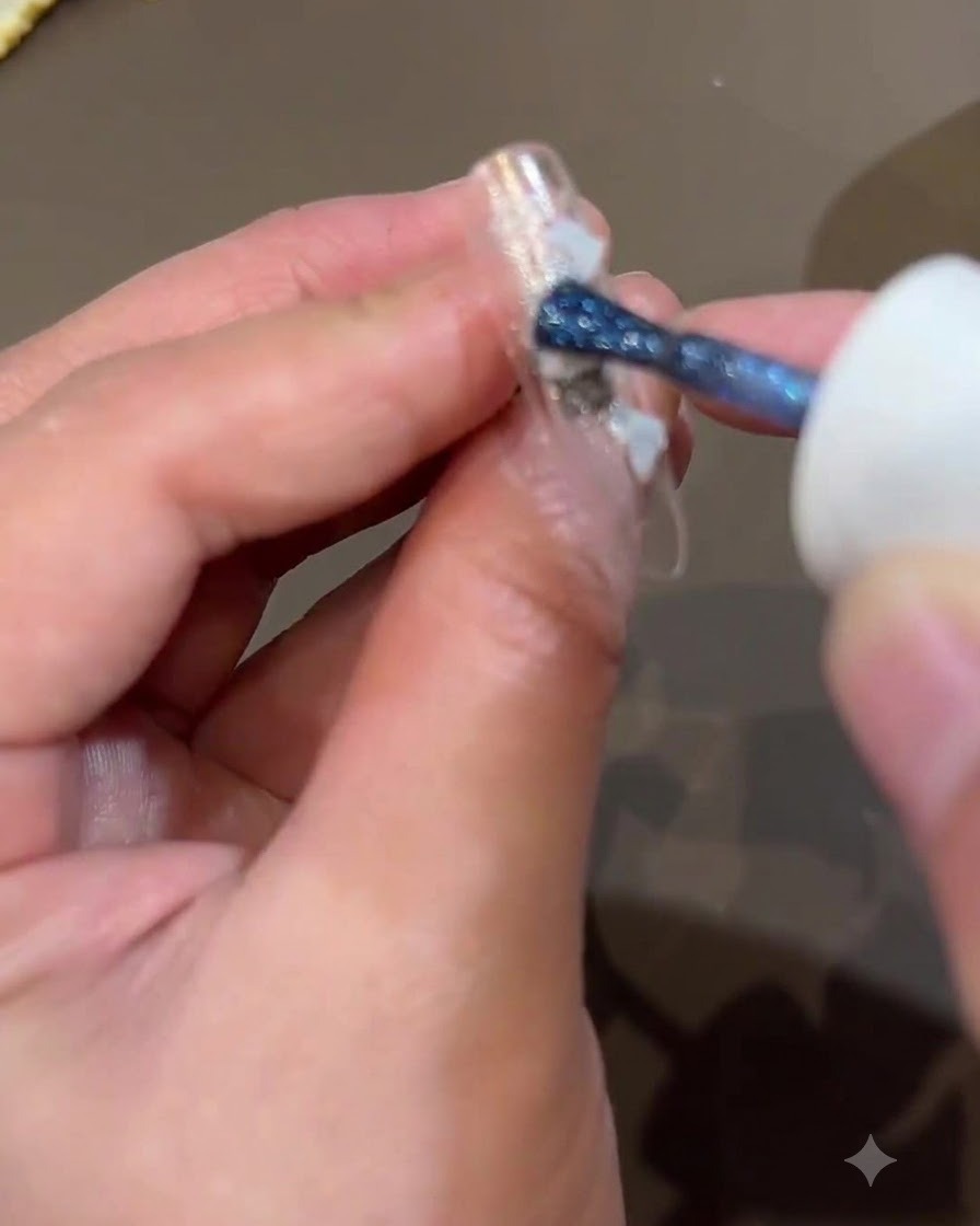 A brush applying dark blue shimmer onto the nail surface to add depth to the design.