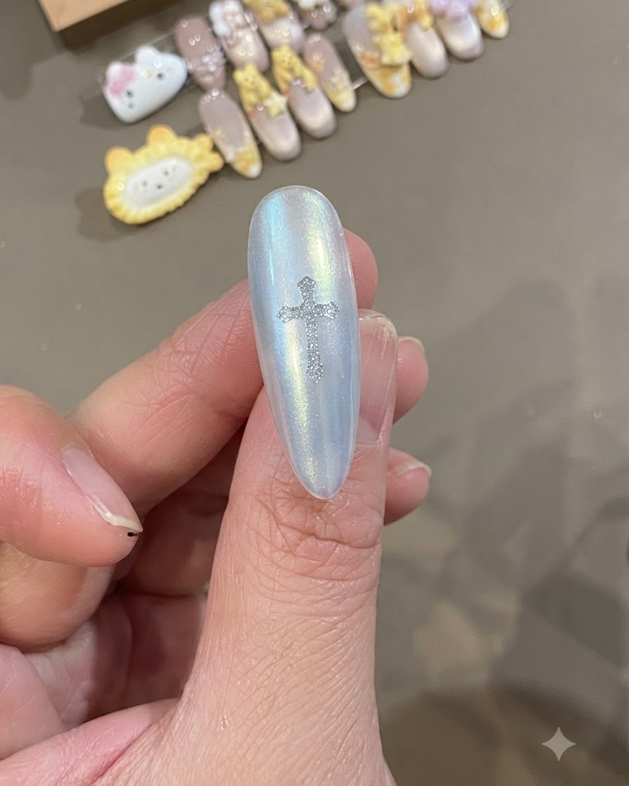 A close-up of a pearlescent white nail with a sparkling silver Chrome Heart cross sticker placed directly in the center.