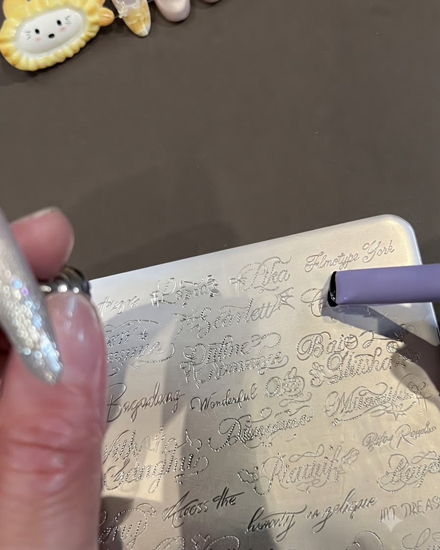 A close-up of a metal stamping plate engraved with cursive English words and a purple jelly stamper picking up the design.
