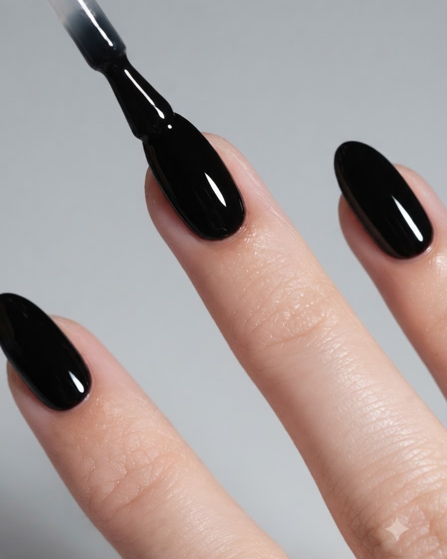 A close-up of a brush applying glossy black gel polish to an almond-shaped nail.