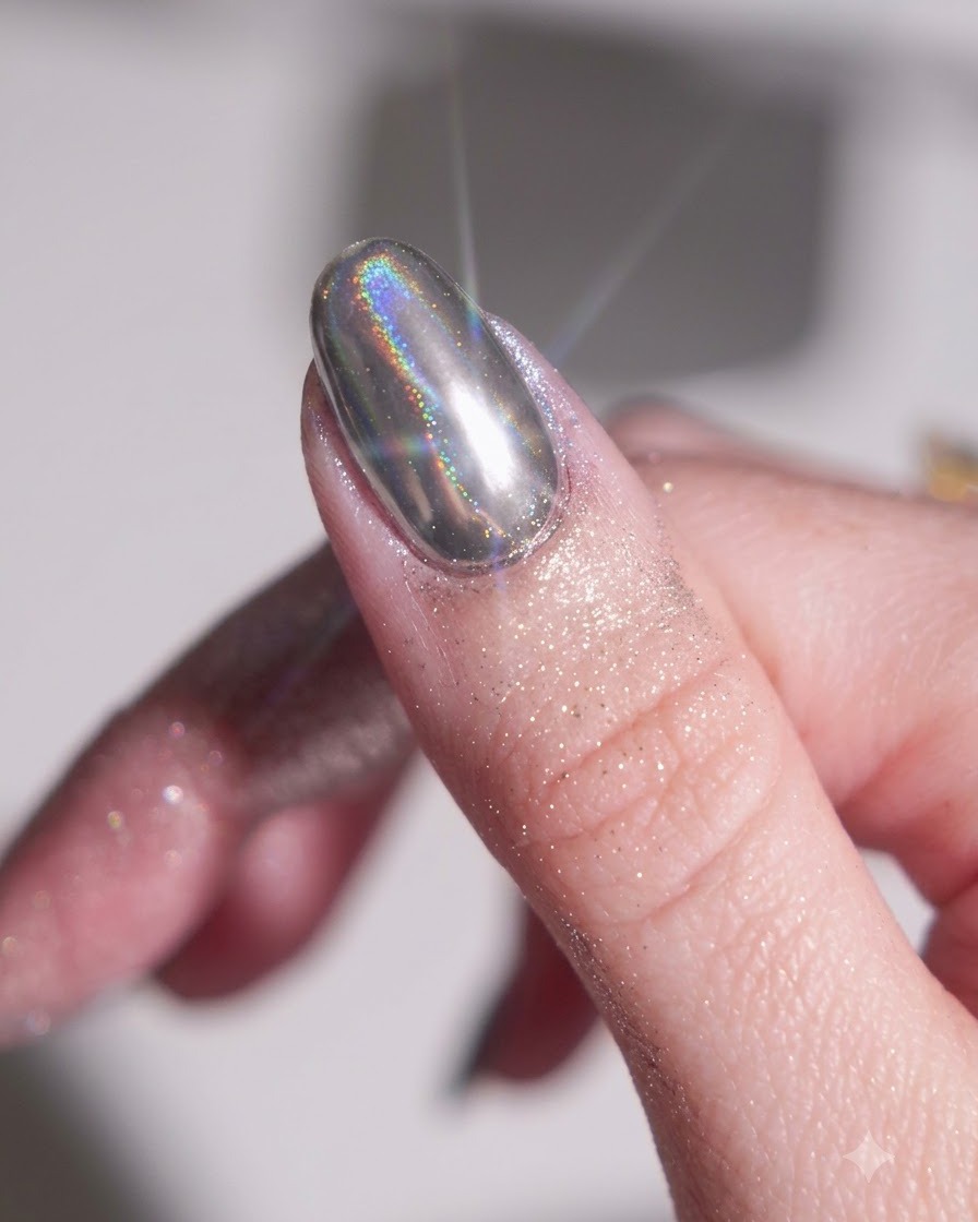 A finger with a cured black base gel being rubbed with a silver chrome powder using a silicone sponge applicator.