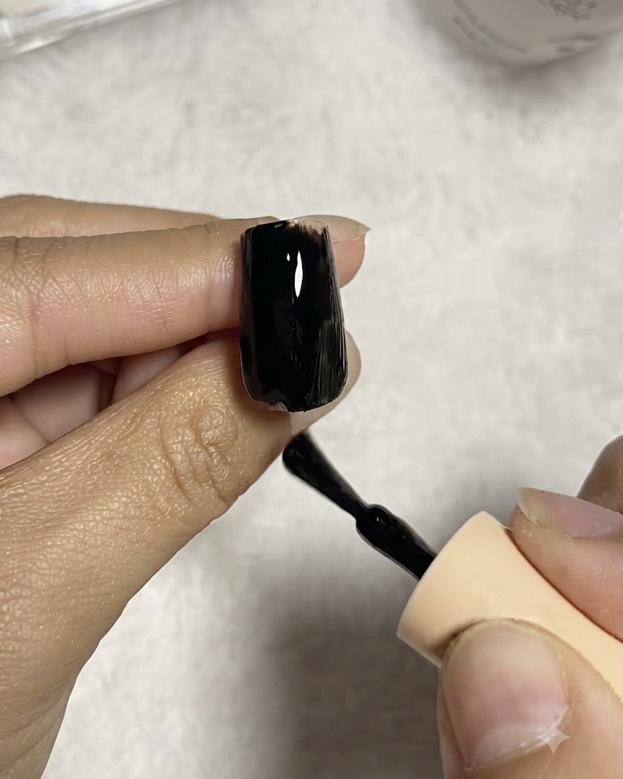 A nail brush applying a smooth coat of black gel polish onto a clear nail tip extension.