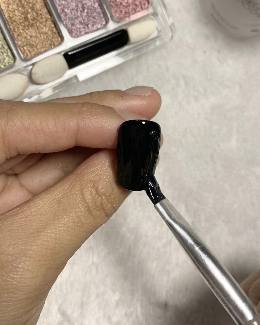 A split-head brush pulling textured vertical lines using clear glue on a black gel nail surface.