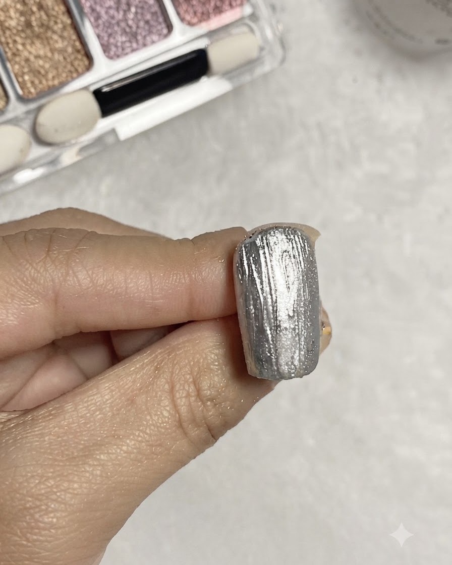 A brush applying clear base gel over a textured silver metallic nail surface.