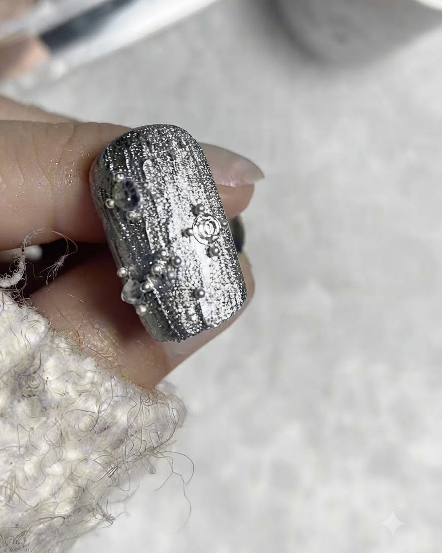 A nail design showing a square steel bead placed centrally with surrounding tiny steel beads.