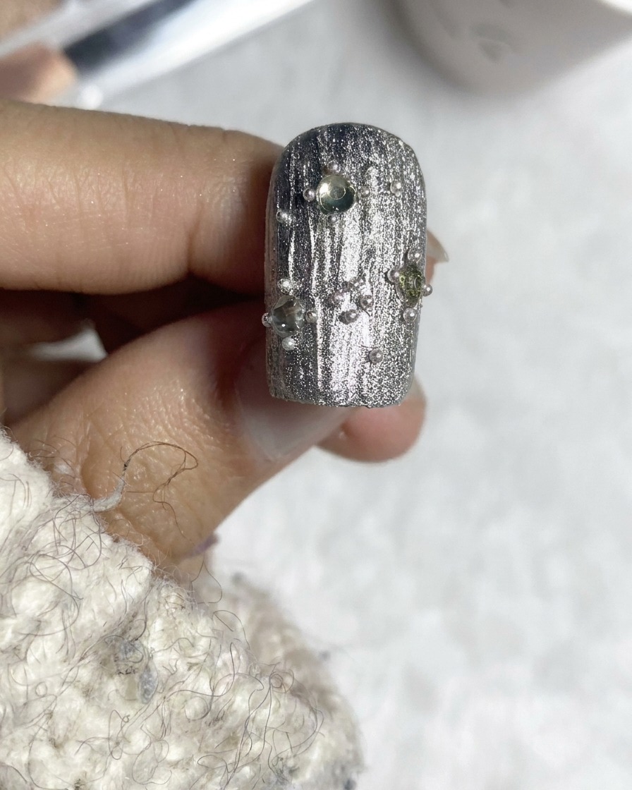A top coat brush finishing an embellished silver textured nail design.