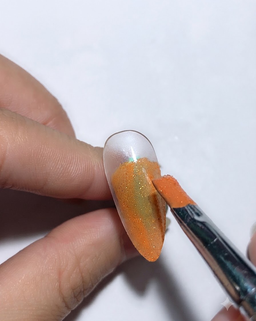 A brush applying starry sky glue over an orange colored nail base.