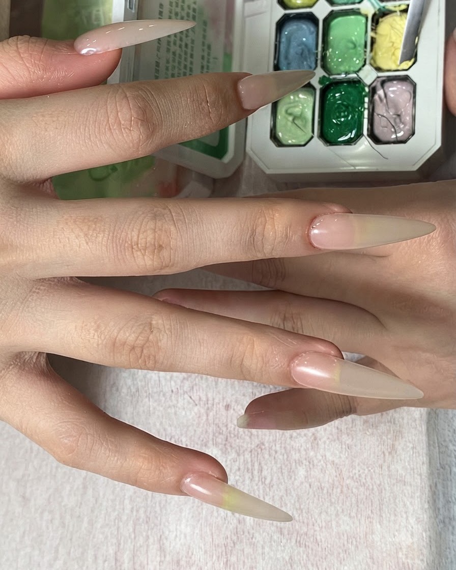 A hand holding a sponge over a color palette, tapping yellow color onto a long nail tip.