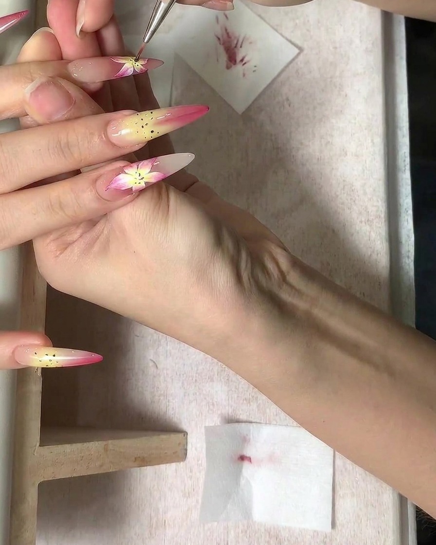 A fine brush adding detailed brown stamen dots to the center of a flower nail design.