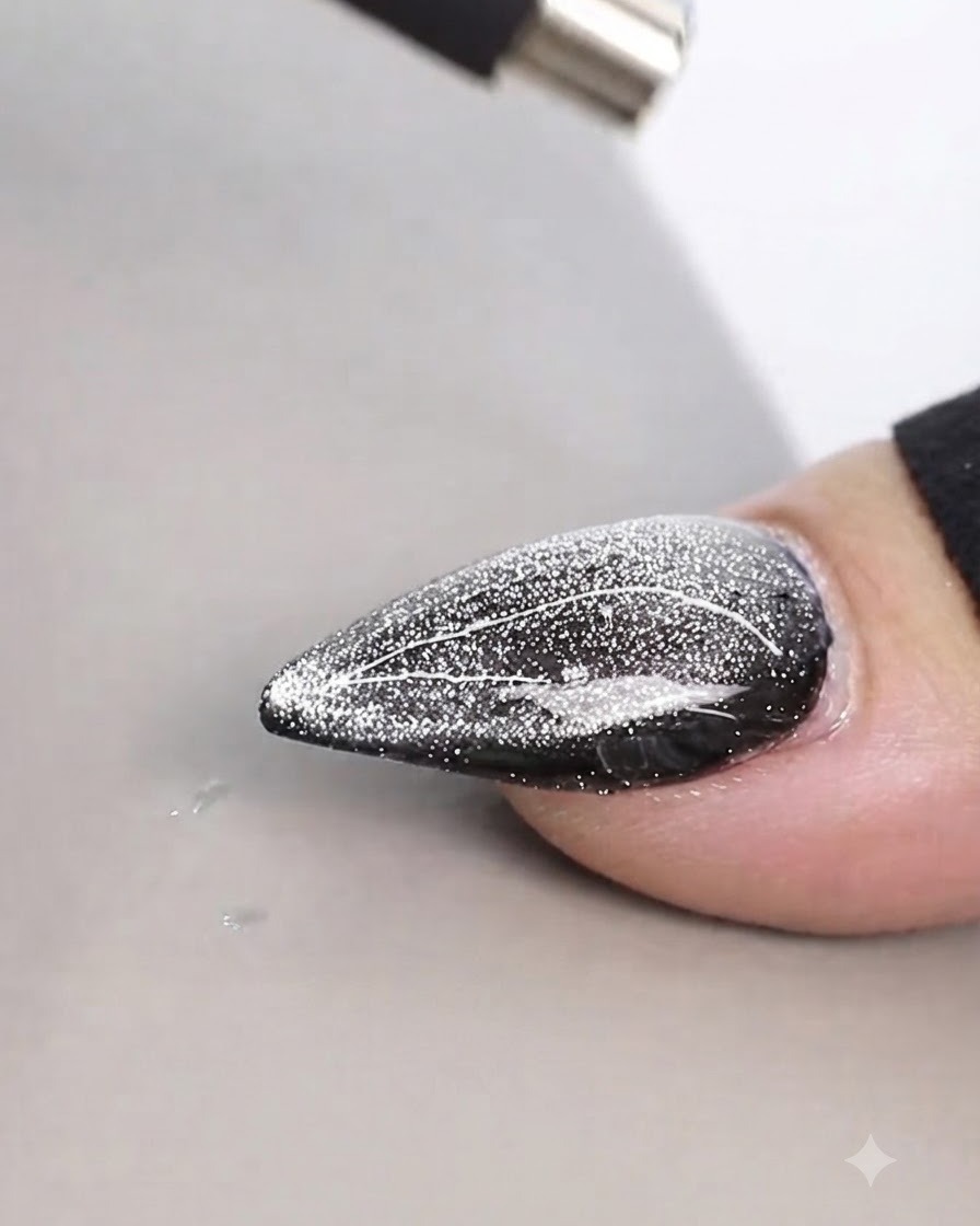 A cylindrical magnet held closely above a shimmering cat eye nail design to create fine lines.